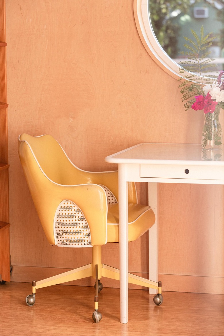 yellow leather desk chair and white small desk with flower vase on top