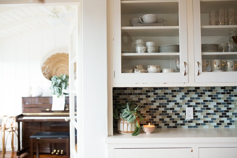 A white kitchen cabinet with dish ware, and a blue-neutral backsplash.