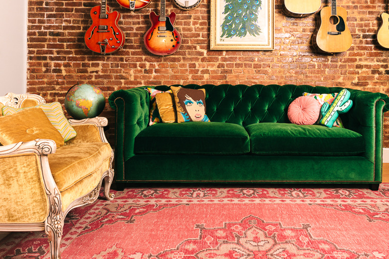 Tufted green velvet sofa in front of red brick wall and rosy area rug