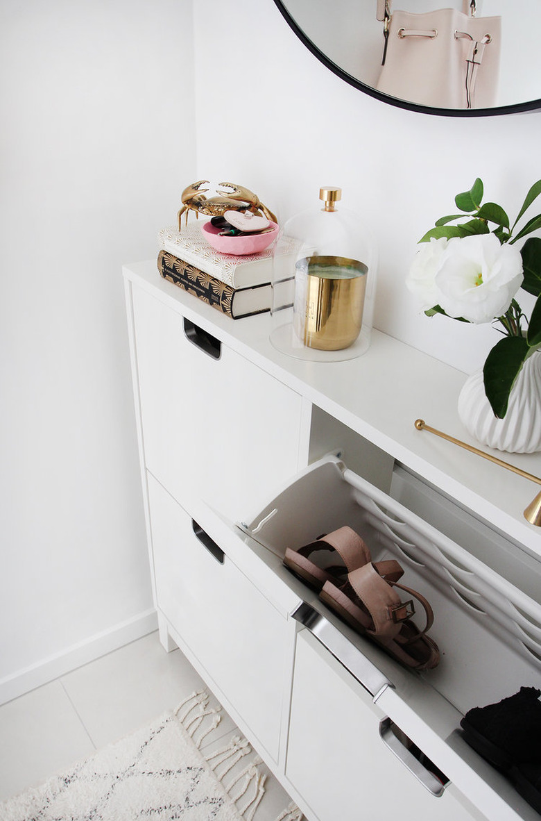 shoe storage cabinet in hallway with round mirror and area rug