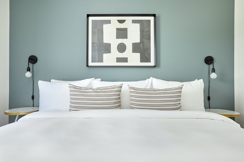 Modern bedroom with bed, white bedding, light blue wall, black sconces, throw pillows.