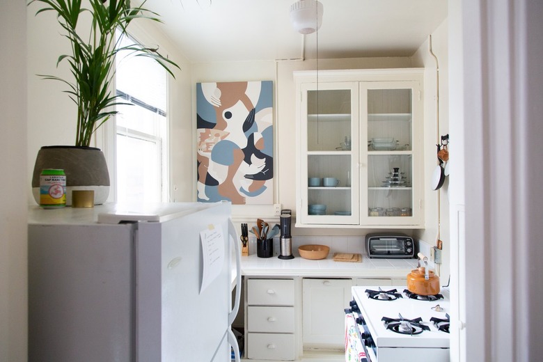 Small white kitchen with windowed cabinets and artwork on wall