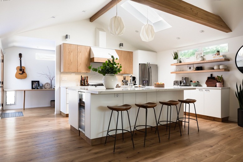 wooden upper kitchen cabinets and lower white kitchen cabinets and modern bar stools with white island and open shelving and wood floors