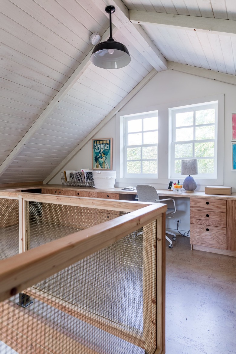 An office loft with a wood-mesh wall. A Scandinavian style wood desk and a black bell pendant light.