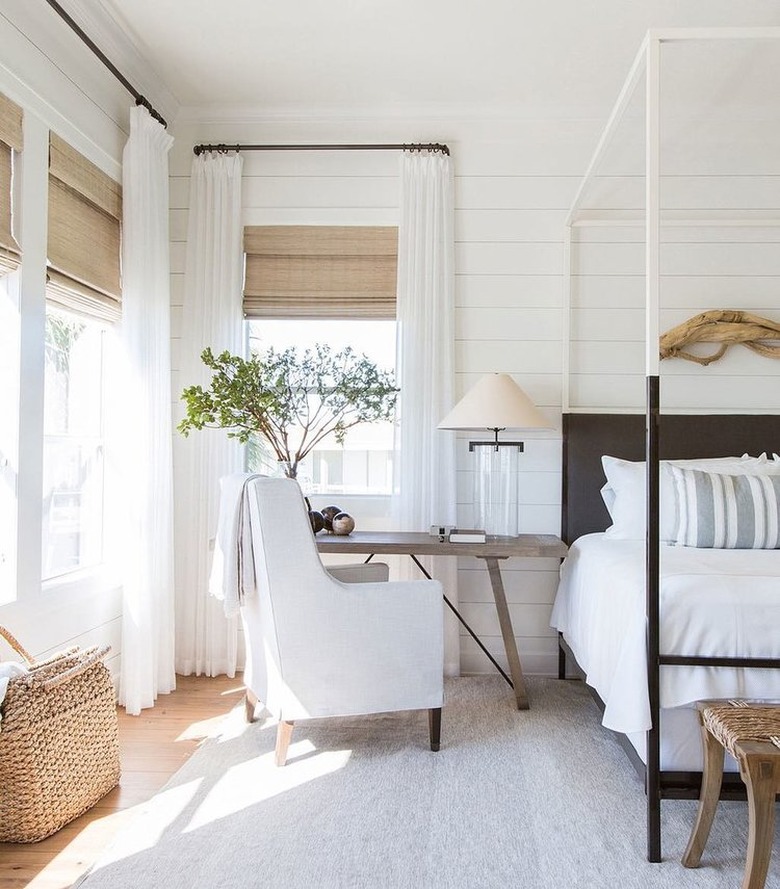 Bedroom featuring white curtains opened around tan woven roman blinds