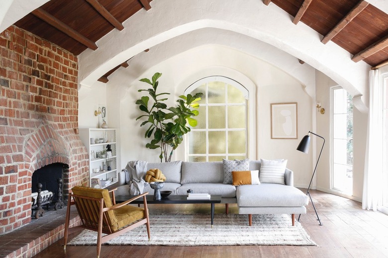 Minimalist living room with wood beam ceiling, red brick fireplace and large fiddle leaf fig.