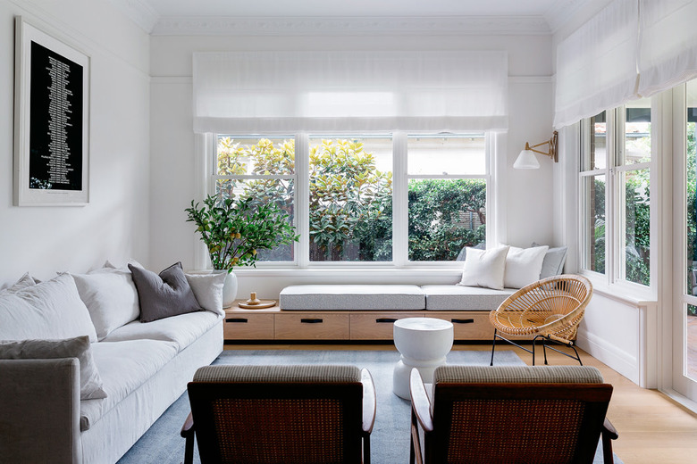 A white-walled living room with big windows, a white couch and linen curtains.