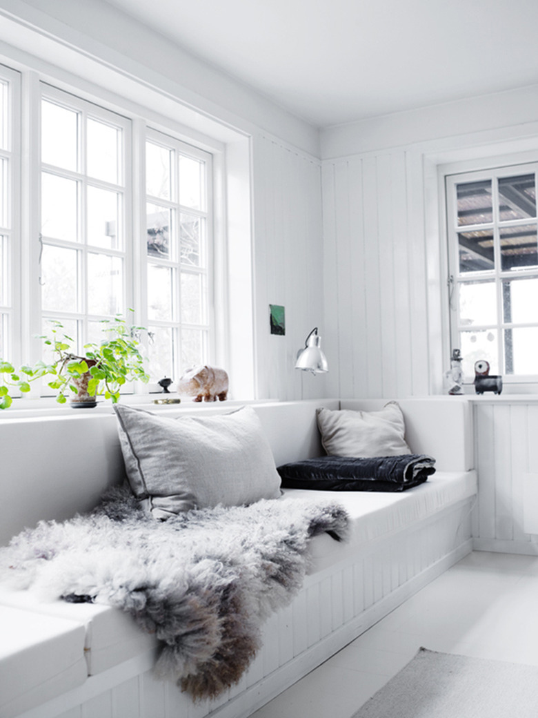 Minimalist living room with built in bench seat, white planked walls and green plants.