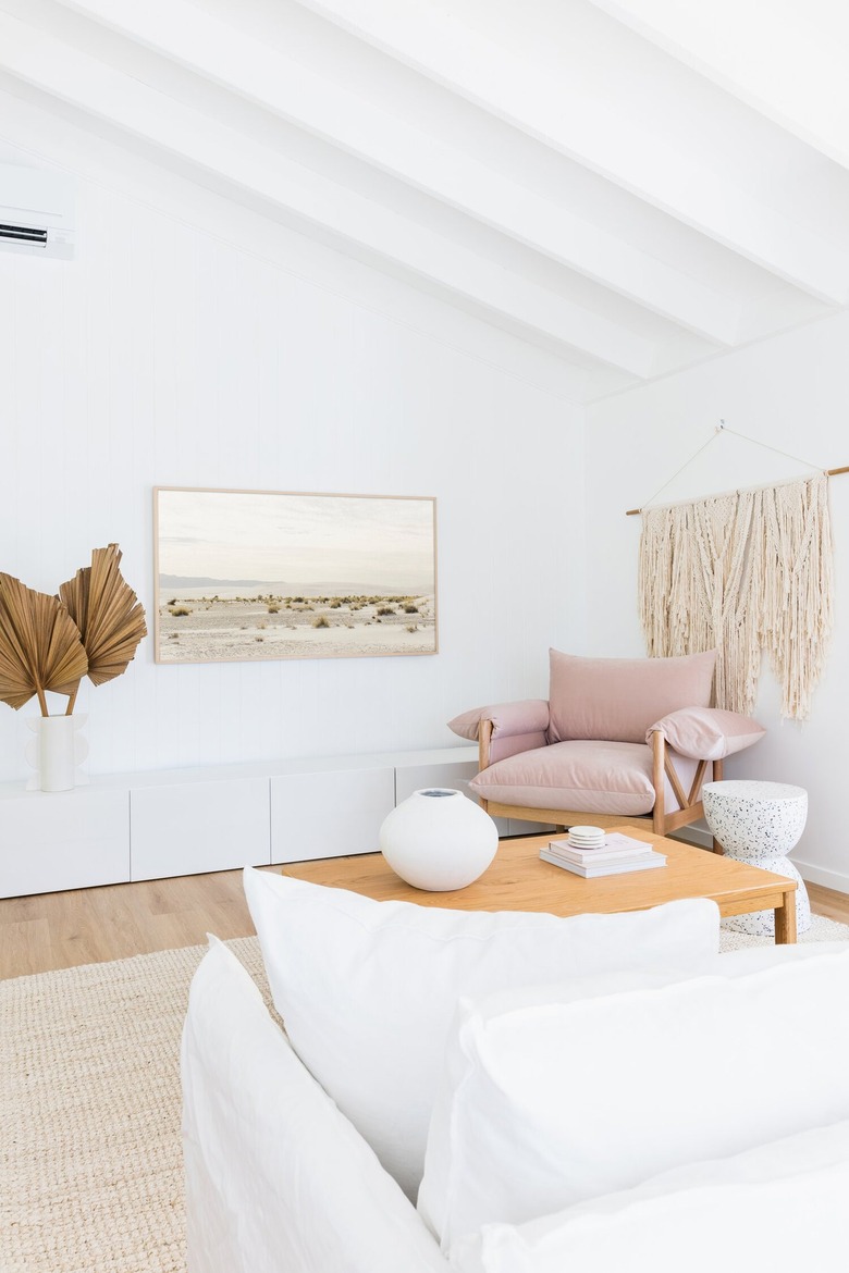 Bright living room with white walls and a white couch, a large macrame wall hanging and pink oversized arm chair.