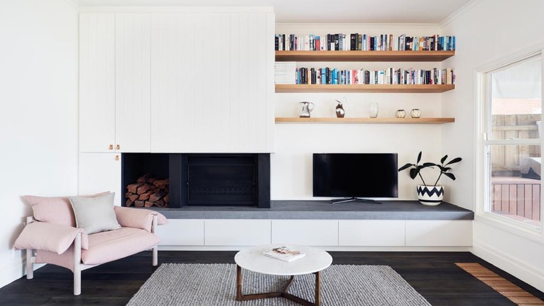 White walled living room with white fireplace and natural wood floating shelves.