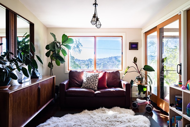 A boho style living room with pillows and fur rug with plants and wood furniture