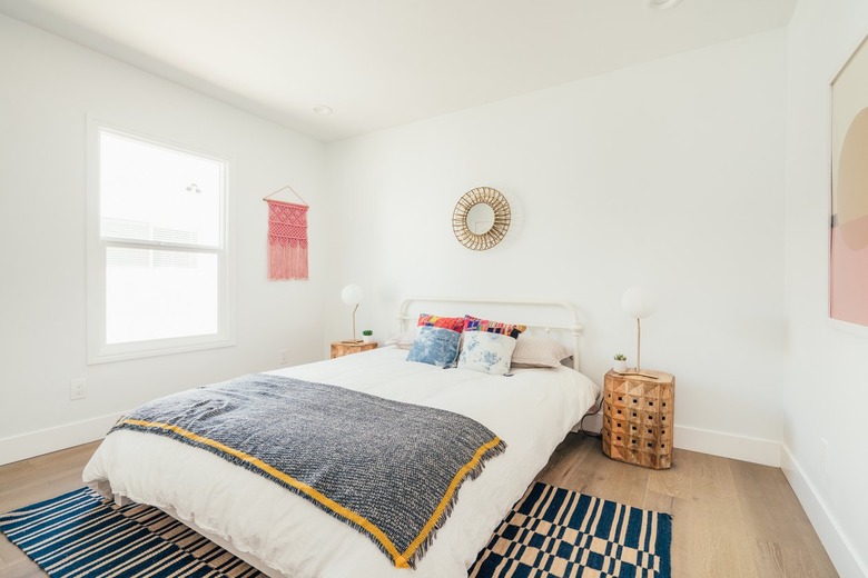 Bedroom with black-white rug, colorful bedding, symmetrical wood nightstands with globe lamps and a sun mirror and macrame