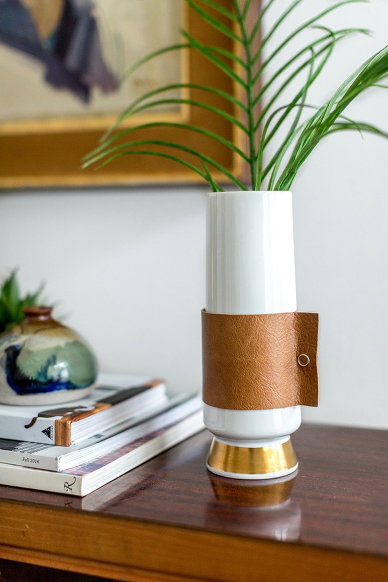 a vase with a decorative diy leather wrap sitting on a tabletop and filled with greenery