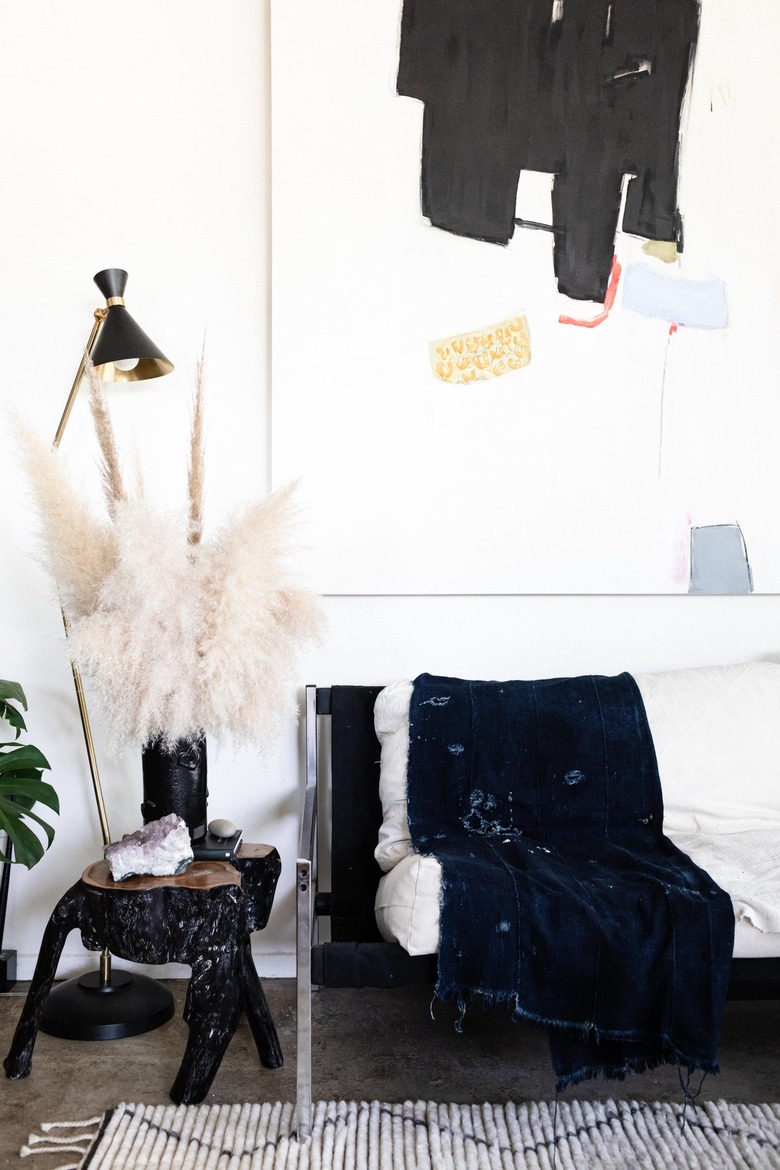 White cushion sofa with a blue blanket, abstract art, striped rug, and pampas grass.