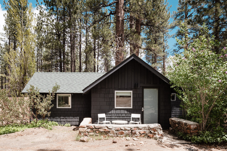 A one-story brown cabin with several trees surrounding it