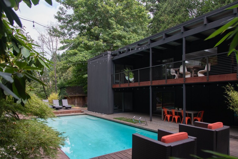 A two-story midcentury home with a rectangular in-ground pool surrounded by patio furniture