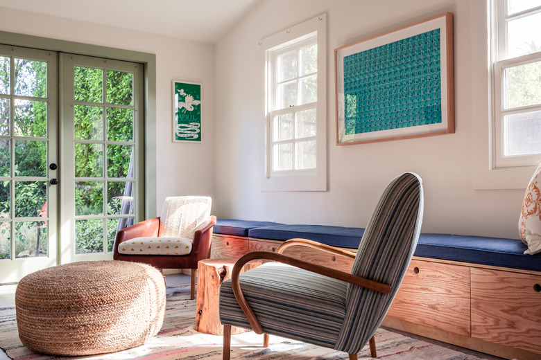 Living room with a blue cushion-wood bench, striped accent chair, leather accent chair, woven ottoman, and French doors.