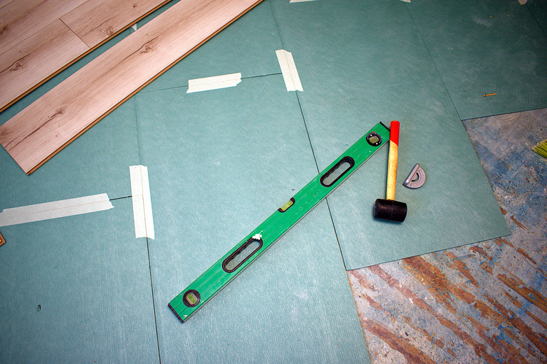 Underlayment for laminate and laminate flooring. Nearby there is a level, a mallet and a corner.