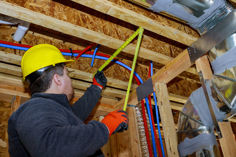 Male builder measuring plastic pipes with new home construction in hot and cold blue and red pex pipe layout in pipes and exposed beams