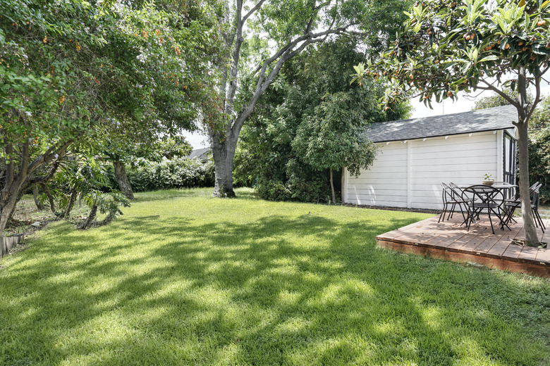 a green lawn with a deck platform; green trees surround a two-car garage