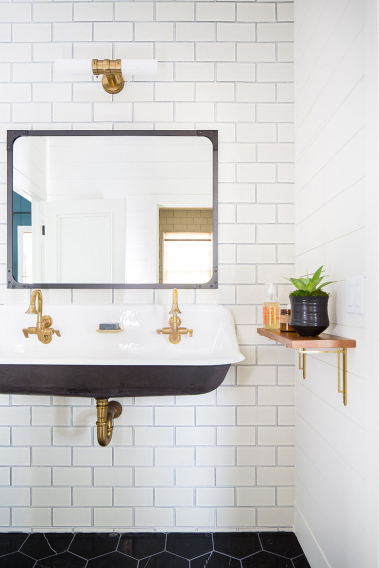 wall-mounted trough bathroom sink on white subway tile with brass fixtures