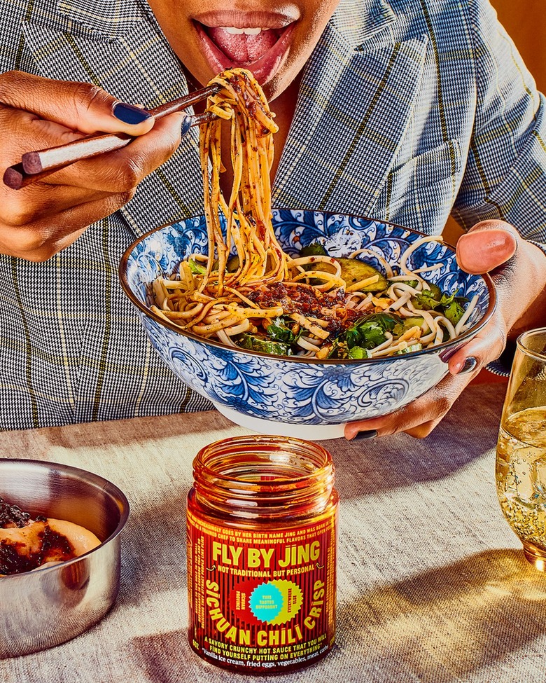 person eating noodles from blue and white bowl with Fly By Jing bottle of chili crisp nearby