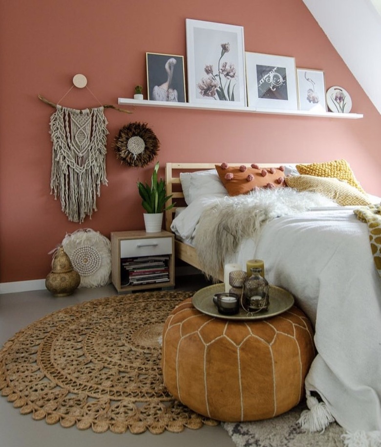 Bohemian bedroom with picture ledge shelf, macrame wall hanging, leather floor pouf, and burnt orange colored paint.