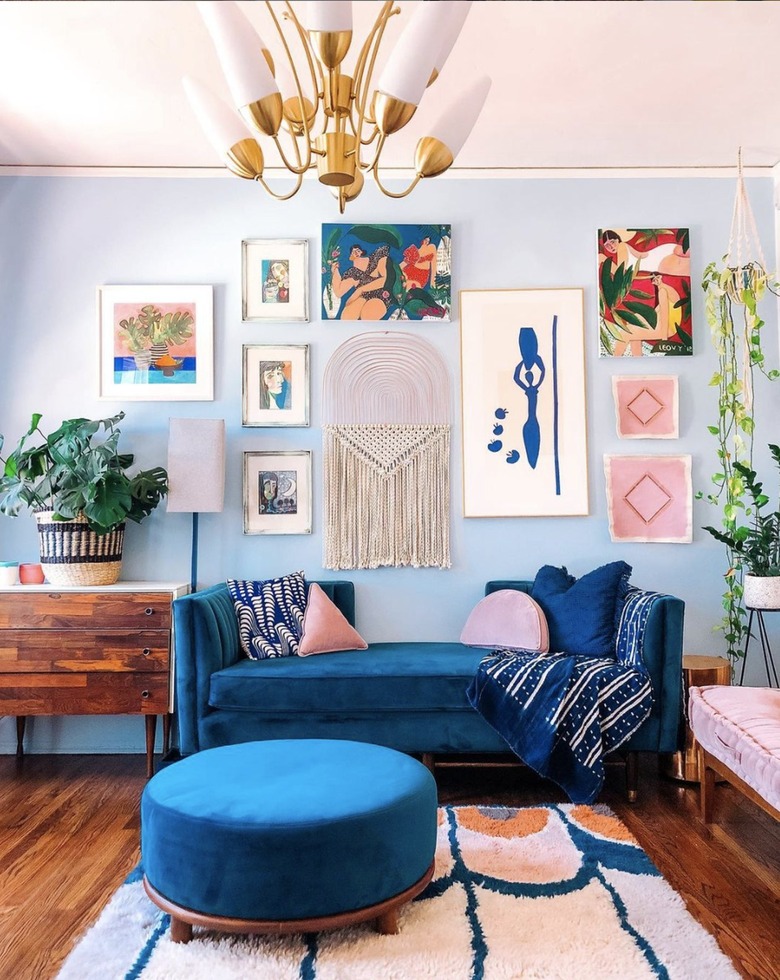 Eclectic living room with light blue accent wall, gallery artwork and bright blue sofa.