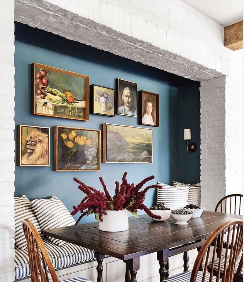 Kitchen nook with wood table, bright white brick and blue green paint behind a gallery wall.