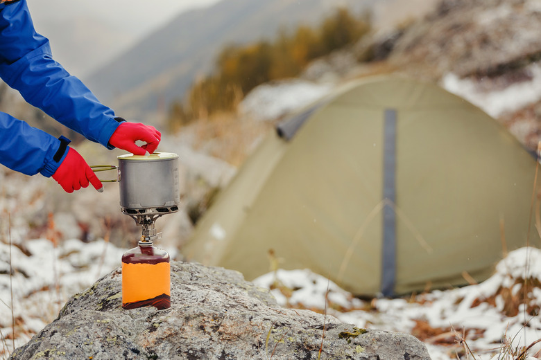 gas cartridge camping jet stove with modern titanium pot on it on a background of the tent during hiking