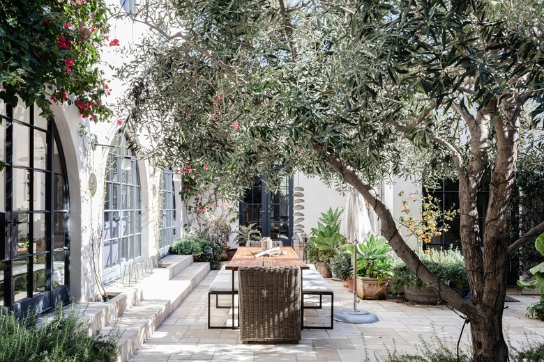 Mediterranean styled patio with trees and plants and a home with large arched windows