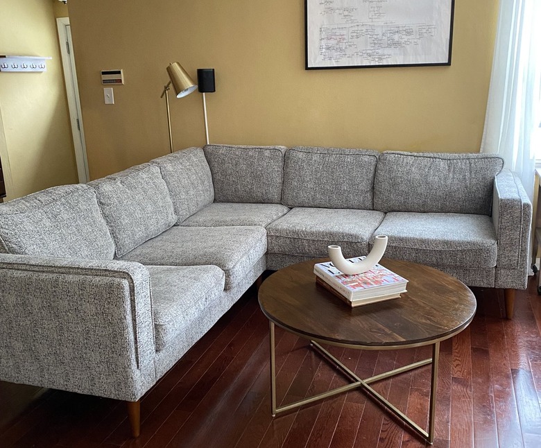 A gray sectional in a yellow living room; a brown round coffee table with books and a decorative vase on top