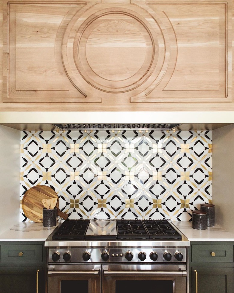 Brass, black, and white art deco backsplash with geometric shapes alongside green cabinets