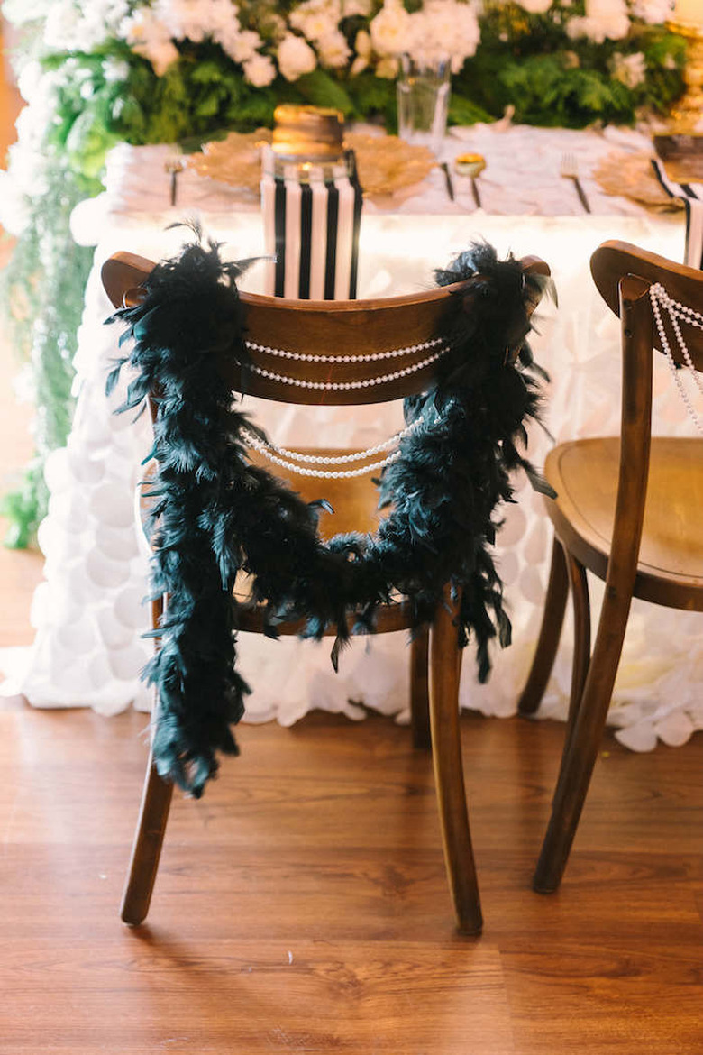 art deco themed party idea with feather boa and pearls draped along back of chairs