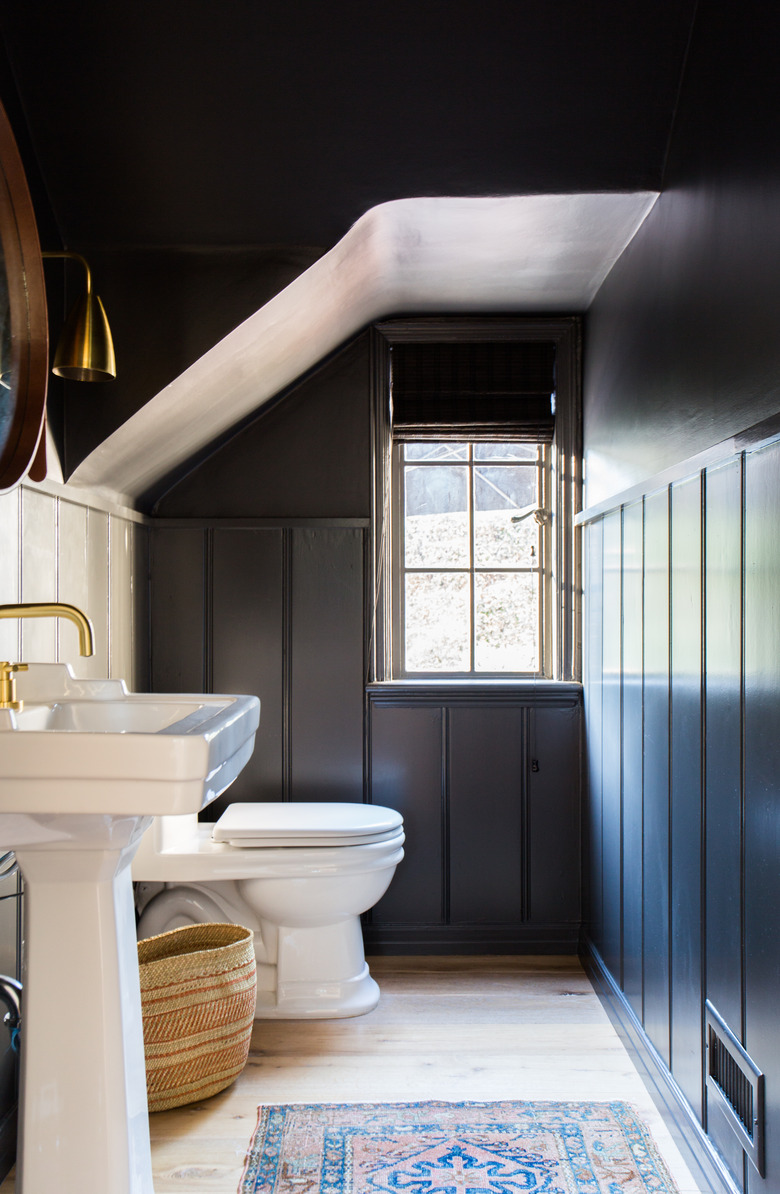 attic apartment bathroom with B=black walls, toilet, sink, brass fixtures, rug.