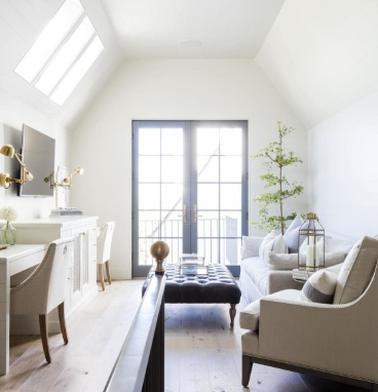 attic apartment with skylights, neutral chairs, black leather ottoman, french doors, wood floors, plant.