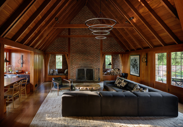 Wood beamed a-line ceiling, black sectional, modern pendant light, and brick fireplace in attic apartment