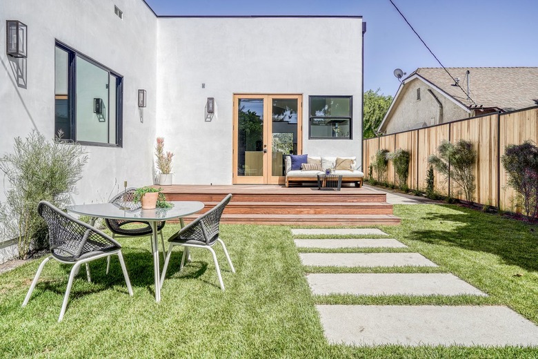 Modern gray house with varying window sizes and casement door. A wood deck with seating. Patio furniture beside a square concrete path.