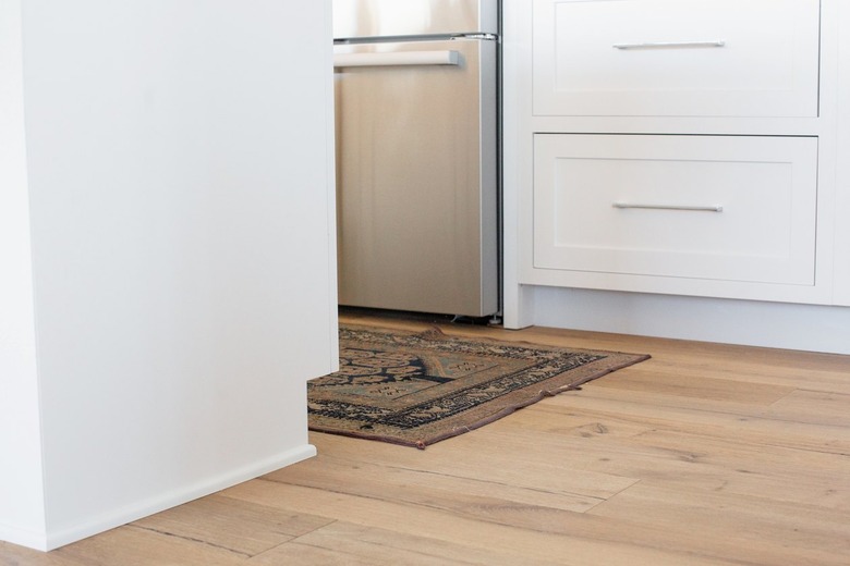 Wood floor, rug, and bottom of white cabinet drawers in a kitchen. Stainless steel oven is visible