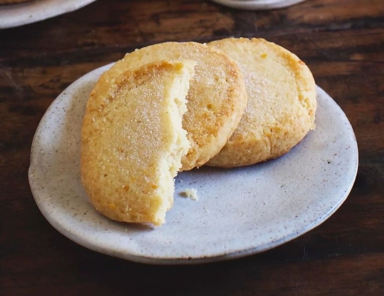 Plate of sugar cookies on a ceramic plate resting on a wooden table. The top cookie has bites taken out of it so it's only half.