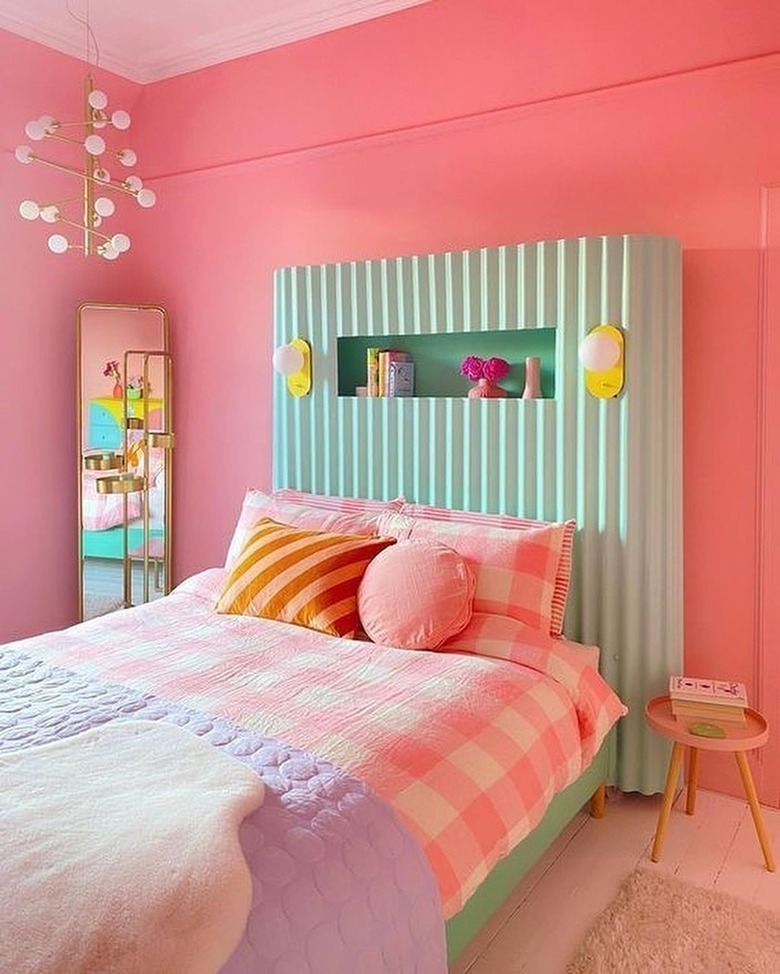 Bedroom with green accent wall, pink bed, and gold light fixture