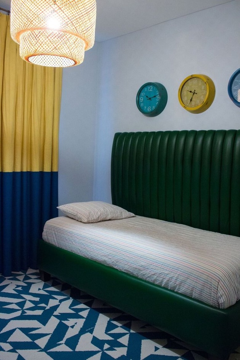 Blue and white tile floors, yellow and blue color block curtain, light cane pendant lamp, trio of clocks on wall, green leather day bed, striped bedding. Basement Bedroom Ideas