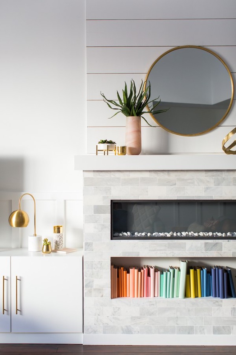 basement fireplace below white brick mantel with gold circle mirror and decorative plant