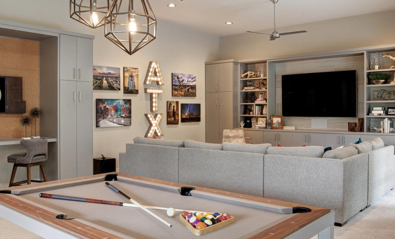 basement game room ideas with gray sectional couch, pool table, walls, flat screen tv bookshelves, pendant lights.