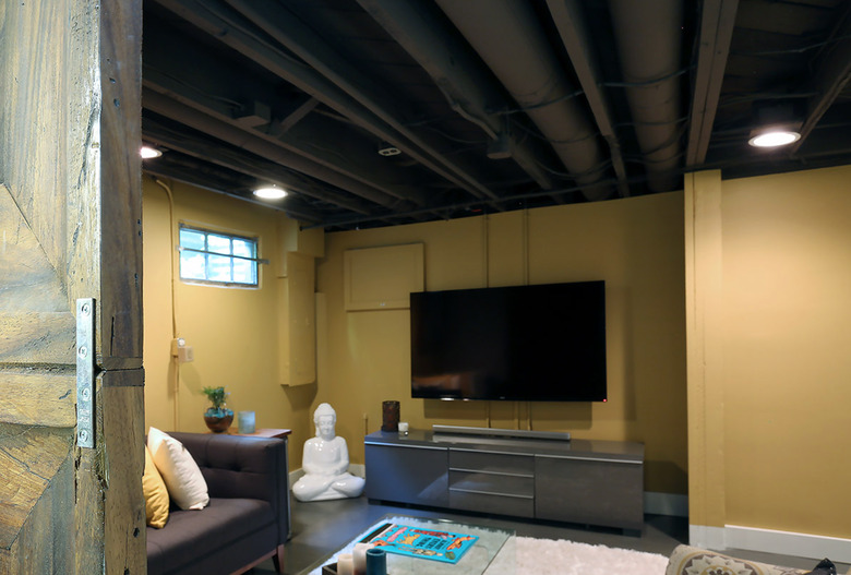 basement lighting in basement with yellow walls, dark gray couch, white area rug, big screen tv, and gray console