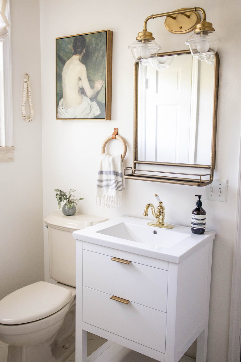 Bathroom with white sink vanity, brass light and mirror, vintage oil painting, wooden towel ring and artisanal beads on hung on wall