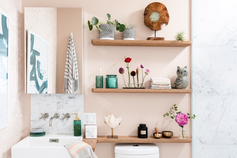 Bathroom with pink walls and wood shelving with flowers and plants