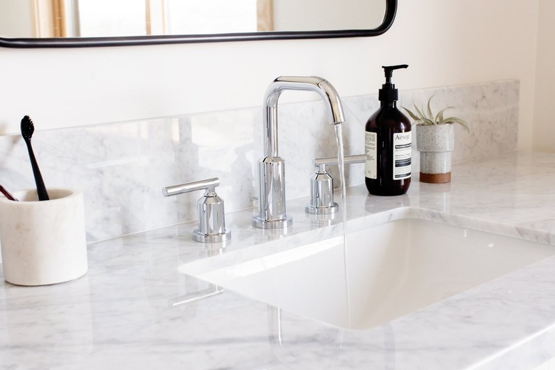 Silver faucet sink with granite or marble countertop. White container with toothbrushes, black bottle, and succulent. Mirror is above.