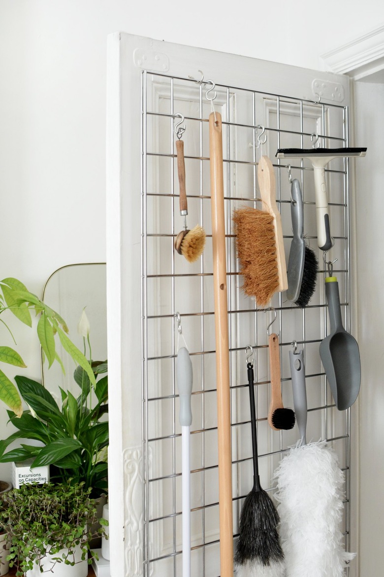 cleaning supplies such as brushes and a squeegee hang from metal hooks attached to a metal grid on a door