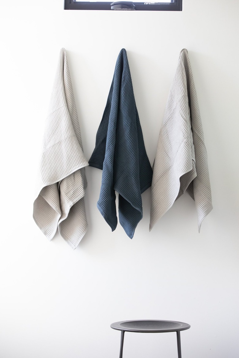 Gray and white towels hanging from white bathroom wall over a stool